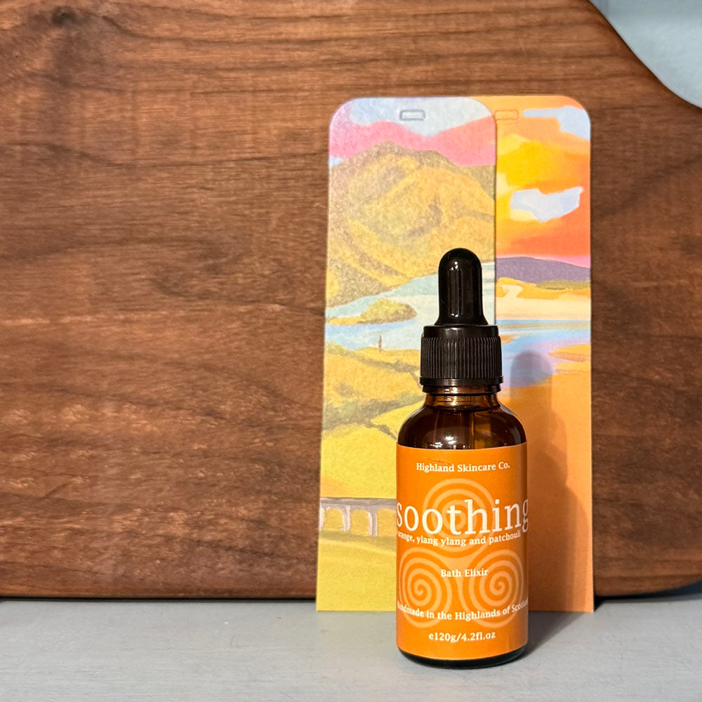 Brown bottle with dropper labeled 'Highland Skincare Co. soothing' next to a colorful landscape box on a wooden surface.