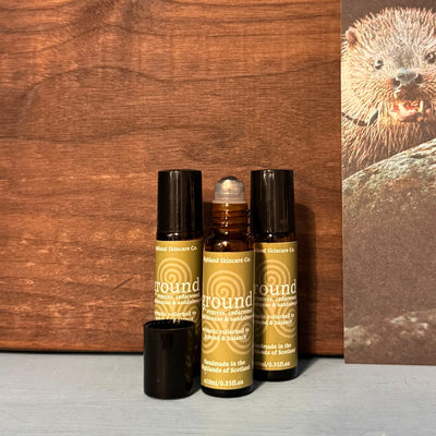 Three bottles of 'ground' skincare products on a wooden surface with a beaver illustration in the background.