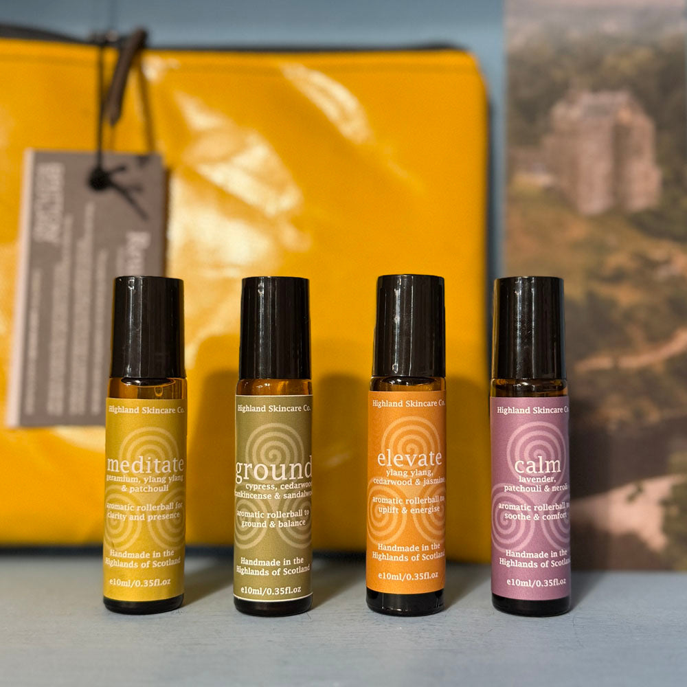 Four roller bottles with labels 'meditate', 'ground', 'elevate', and 'calm' on a surface with a yellow bag in the background.