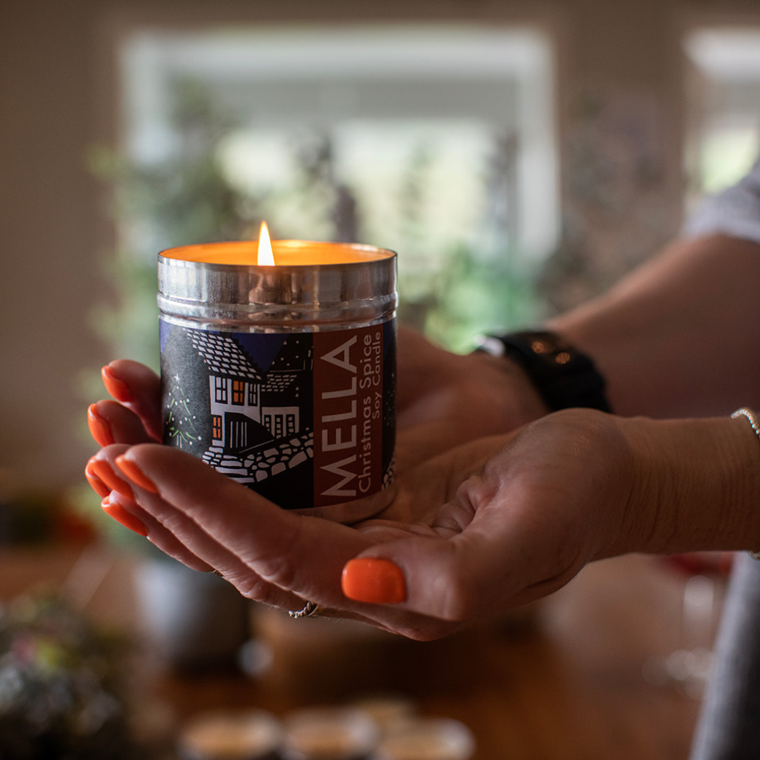 Person holding a Mella candle in a blurred indoor setting