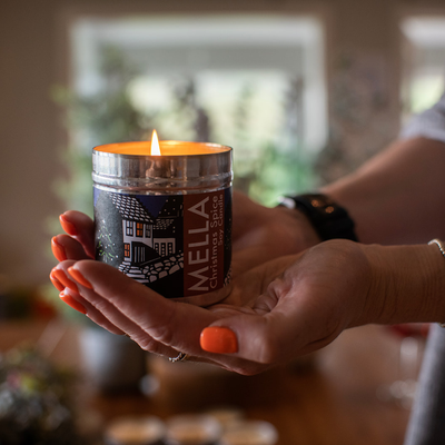 Person holding a Mella candle in a blurred indoor setting