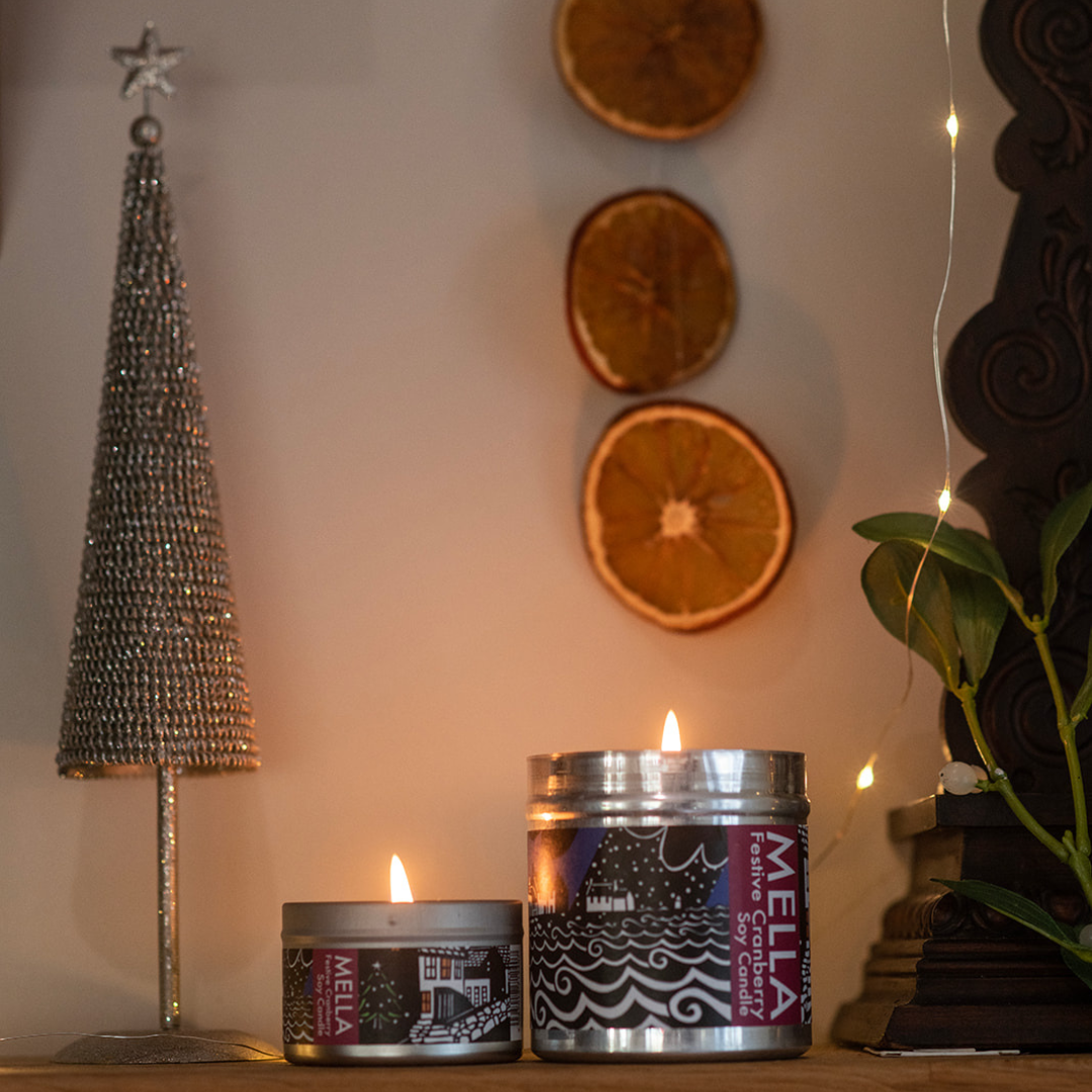 Two Mella candles on a surface with decorative elements including a star-shaped object and dried oranges.