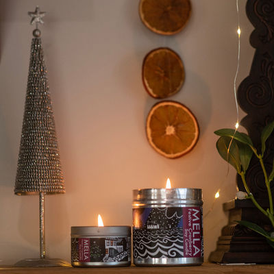 Two Mella candles on a surface with decorative elements including a star-shaped object and dried oranges.